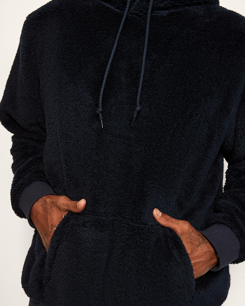 Person wearing a navy hoodie with hands in the pockets on a light gray background