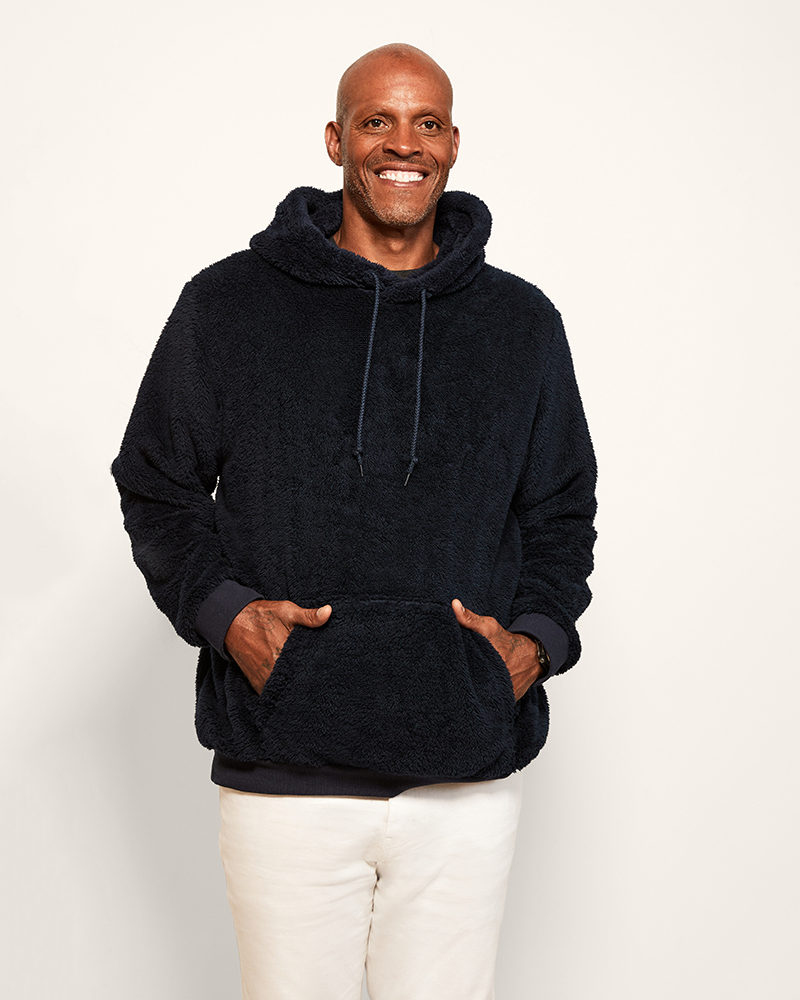 Man wearing a navy hoodie and white pants against a plain background