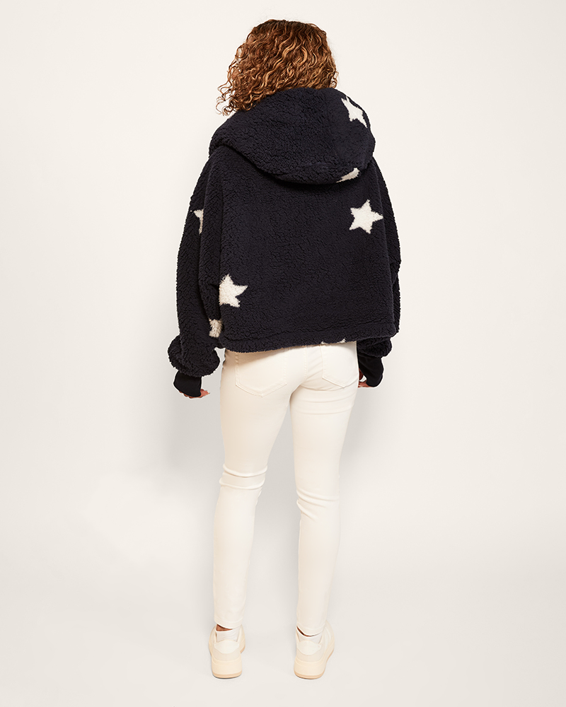 Person wearing a navy hoodie with white star patterns on a plain background