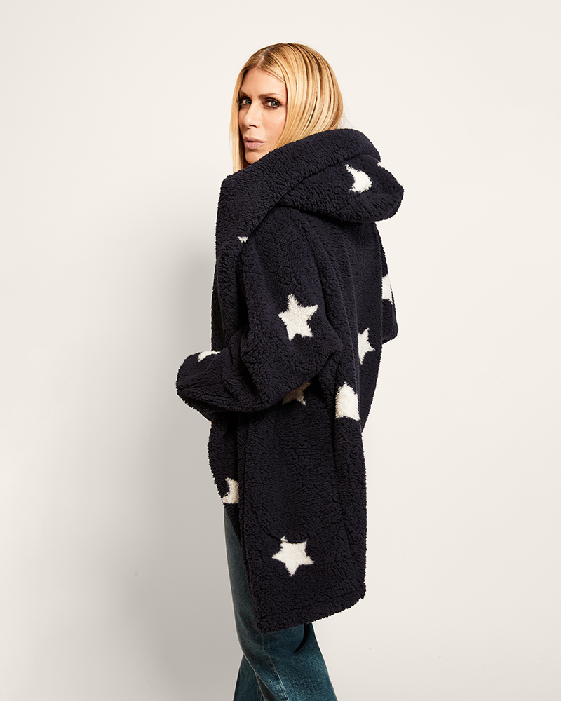 Woman wearing a dark blue coat with white star patterns on a plain background