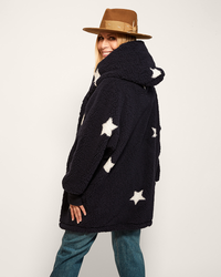 Person wearing a navy coat with white star patterns and a brown hat on a plain background