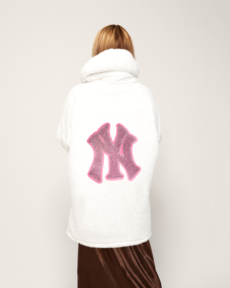 Person wearing a white sherpa lounger jacket with a pink bedazzled yankees logo on the back against a plain background