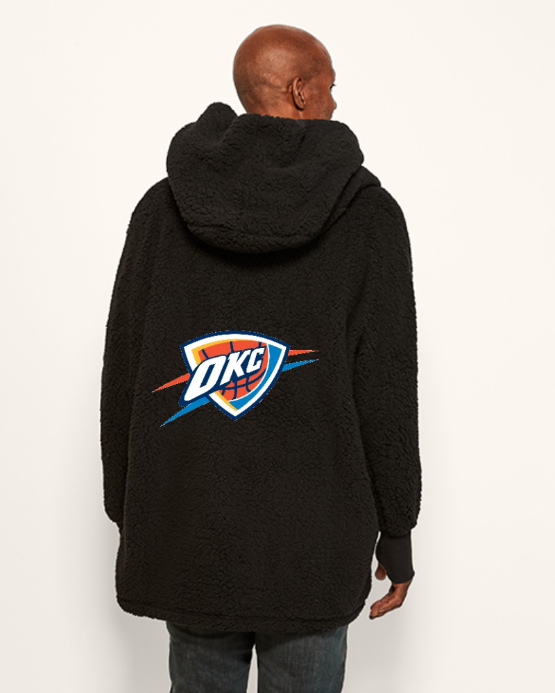 Person wearing a black hoodie sherpa lounger with an OKC logo on the back against a white background