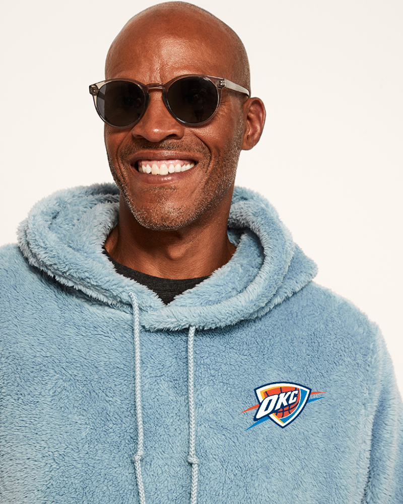 Man wearing a light blue hoodie with a oklahoma city thunder logo on a white background