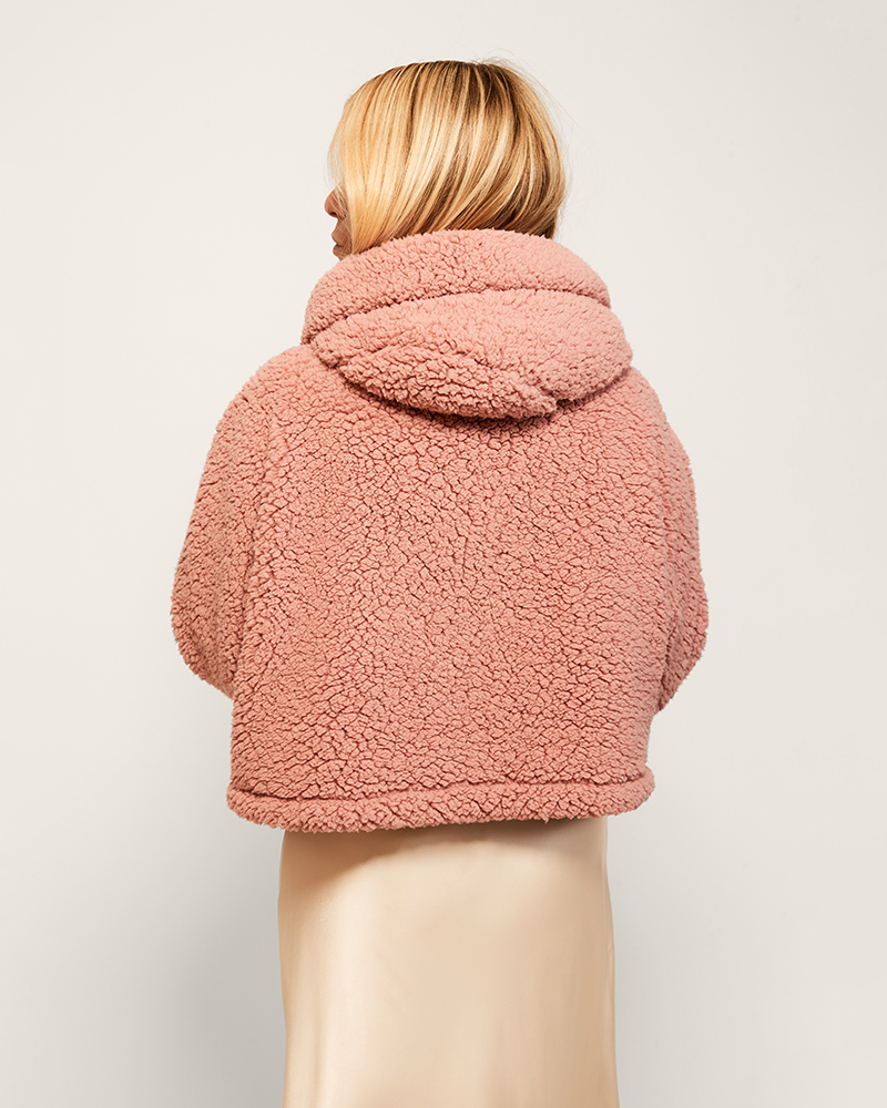 Person wearing a pink sherpa jacket against a plain background
