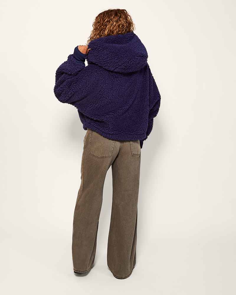 Person wearing a dark blue fleece jacket and brown pants on a white background