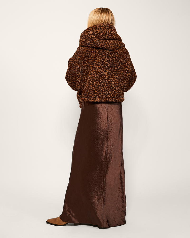 person wearing leopard printed sherpa with hood over brown dress on light background