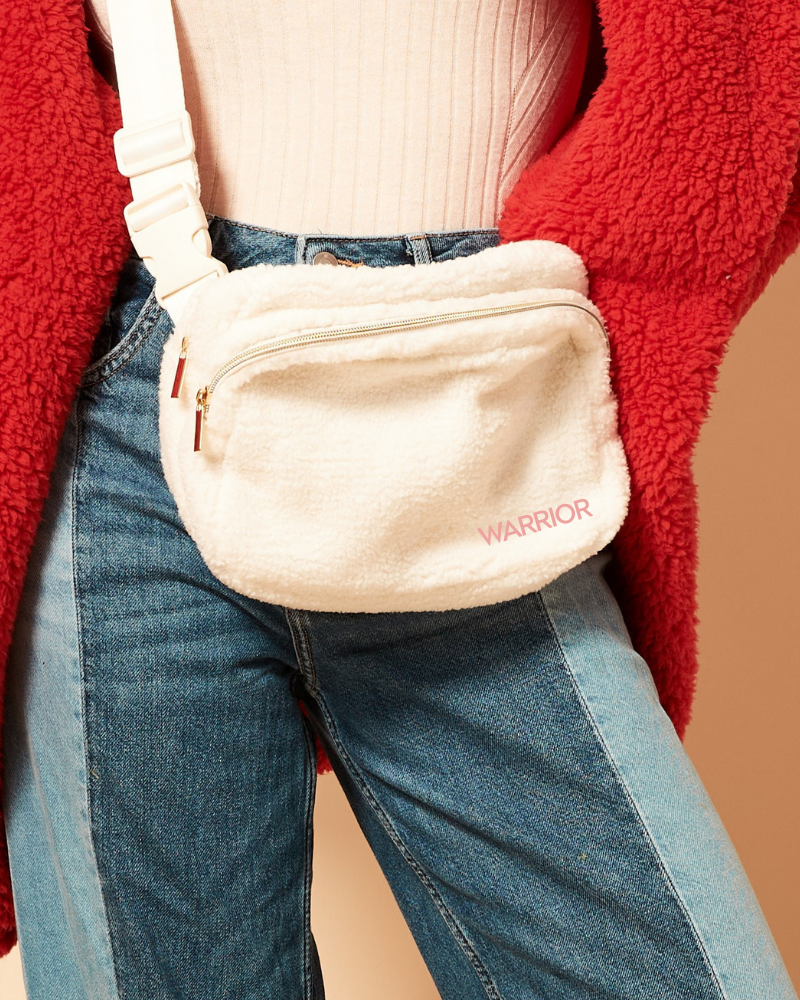 Beige fanny pack with 'Warrior' branding worn by a person in a red jacket and blue jeans.