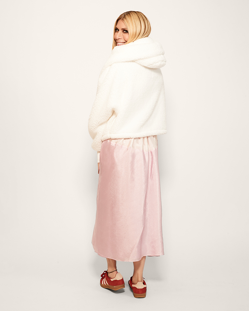 Woman wearing a white lounger jacket, pink skirt, and red sneakers on a white background
