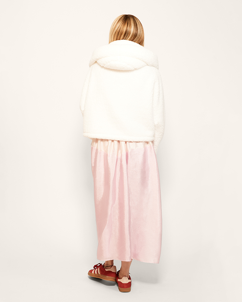 Woman wearing a white lounger jacket, pink skirt, and red sneakers on a white background