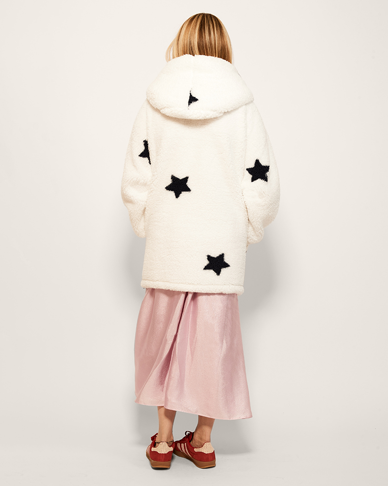 Person wearing a white fur coat with navy star patterns on a light background