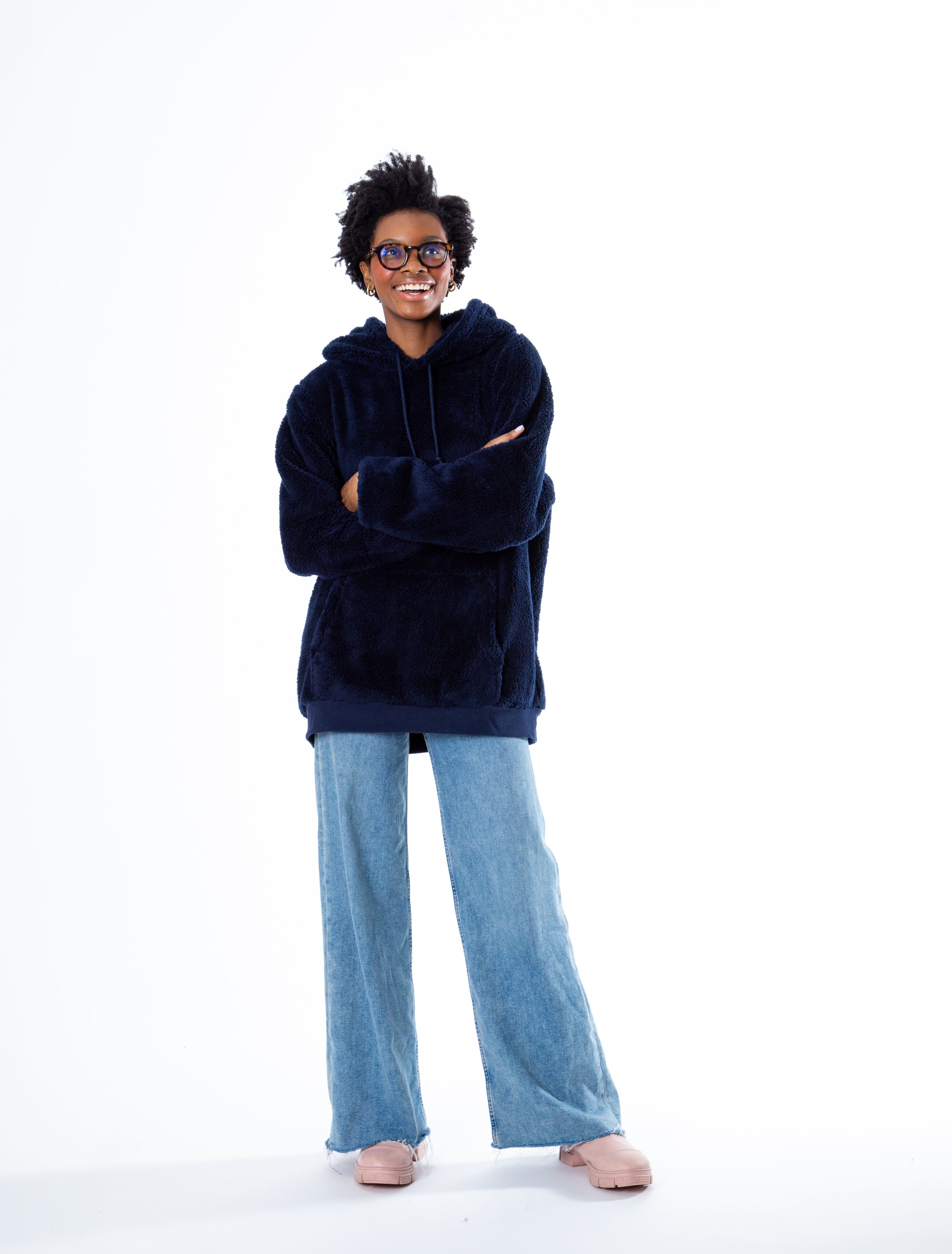 Girl in a cozy navy sherpa sweatshirt and jeans, arms crossed, wearing glasses with a casual, confident look.