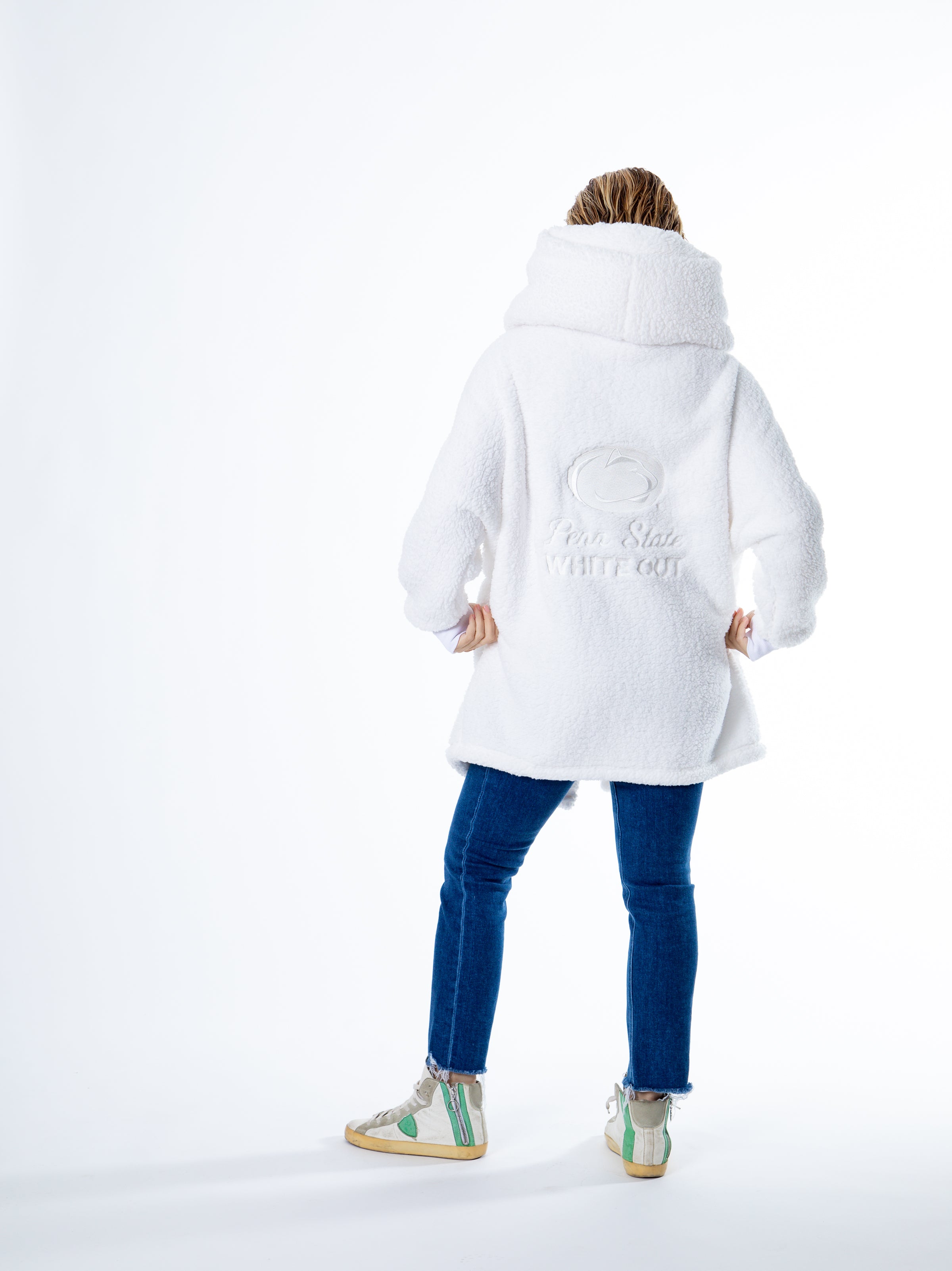 Person facing away, wearing a Limited Edition Penn State White Out Lounger by Jill Martin, blue jeans, and white sneakers with green and yellow accents, standing against a plain white background.
